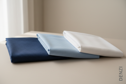 Create a 100% realistic single image featuring three men’s unstitched cotton suits placed neatly side by side. The colors should be Navy Blue, Sky Blue, and White. Show full fabric texture clearly with natural lighting. The background should be simple, clean, and elegant to highlight the suits. Add the text ‘DENZI’ at the bottom-right corner of the picture in a minimal, stylish font should be in vertical direction